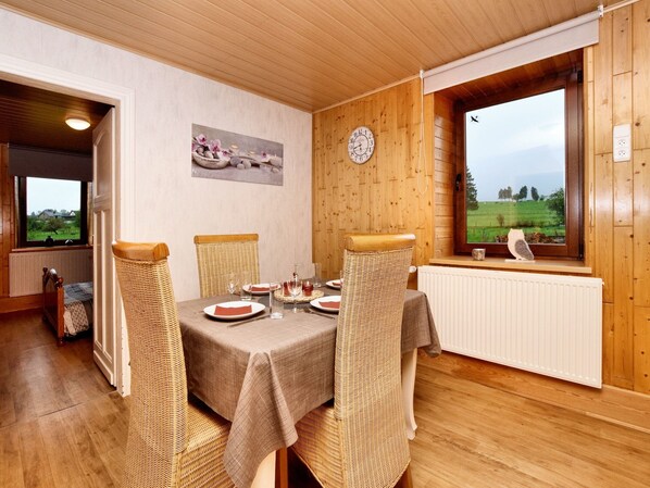 A dining area with a table set for four, wooden chairs, a clock on the wall, and a window with a view of the countryside.