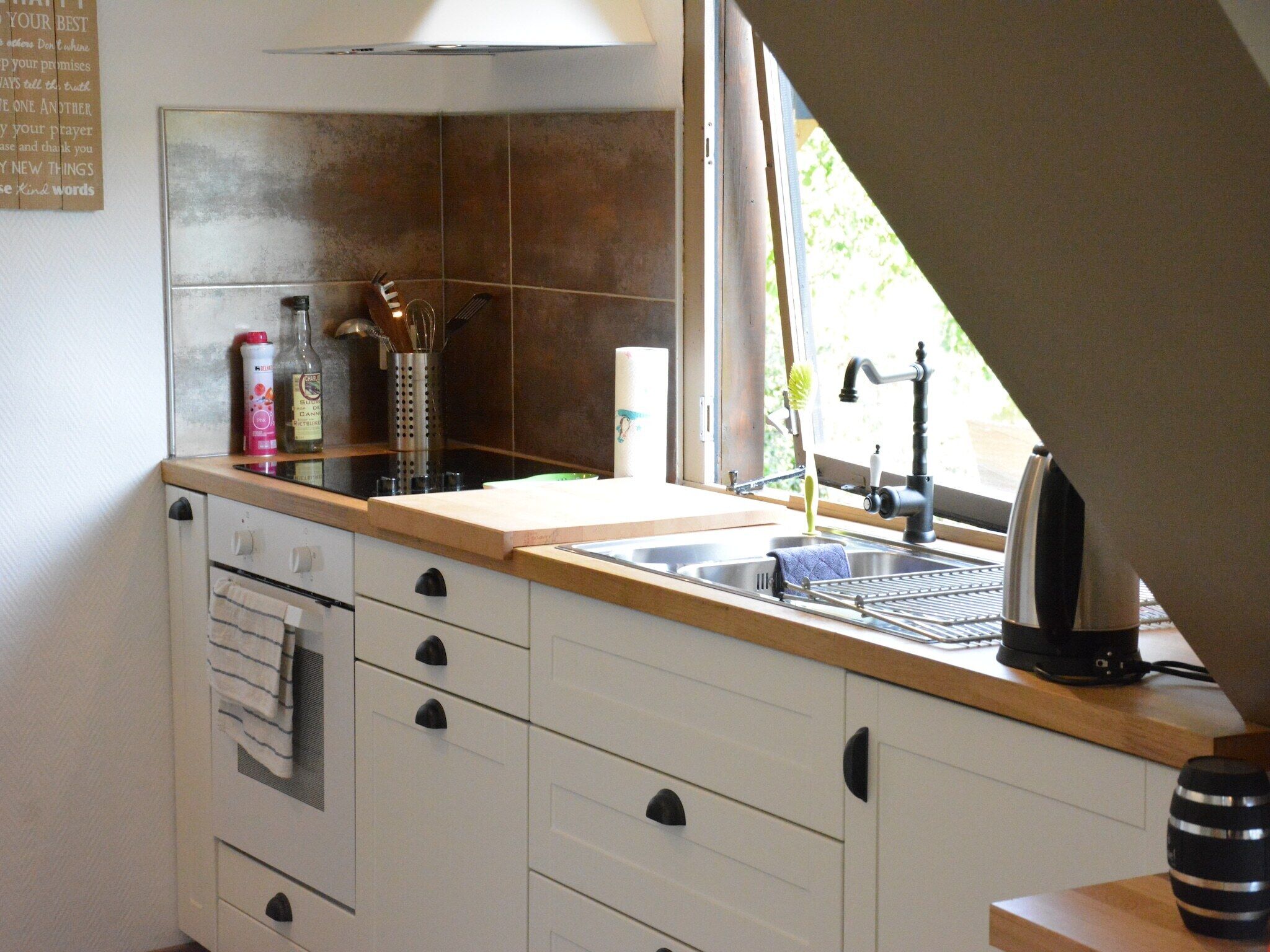 A kitchen with a wooden countertop, a sink, and a window. There are cabinets and a stove.