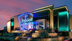 Een modern gebouw met een opvallend 'TopGolf' bord, met een goed verlichte ingang en een trap naar de hoofdingang.