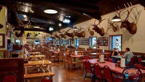 Een restaurant met houten tafels en stoelen, dierenkoppen aan de muur en een groot raam dat uitzicht biedt op een besneeerd landschap.
