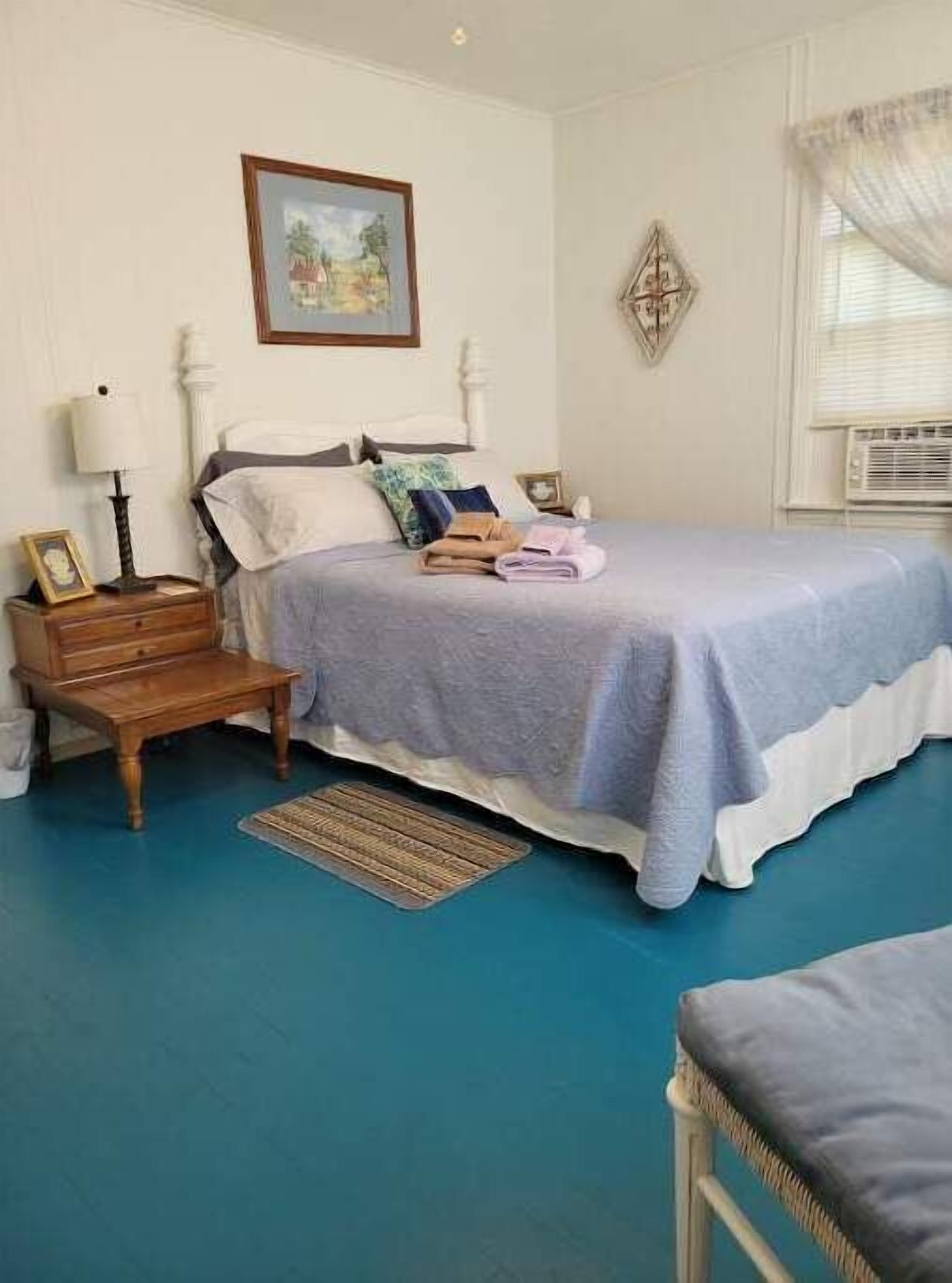 A bedroom with a bed, bedside tables, a nightstand, a rug, and a window with blinds.