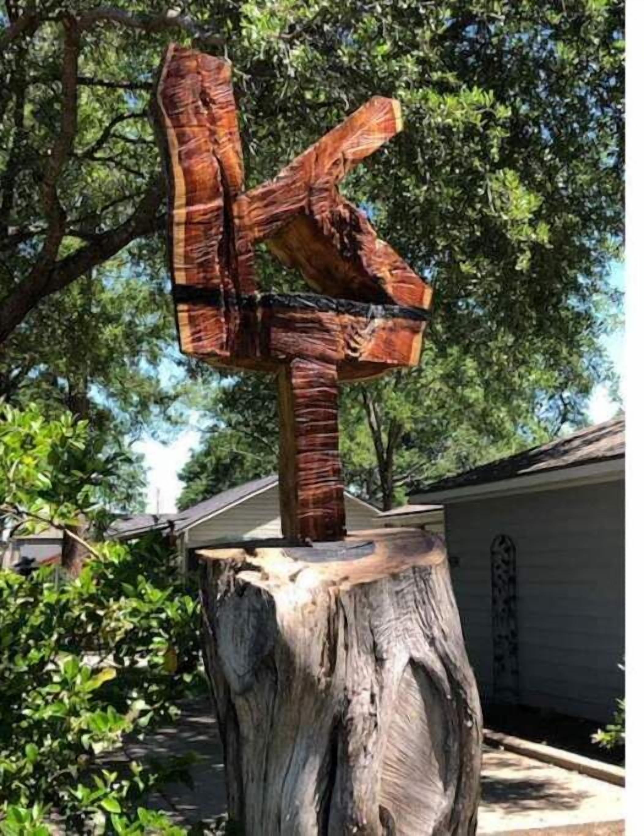 A wooden cross sculpture on a tree stump in a residential area.
