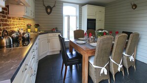 Une cuisine avec coin repas, comprenant un mur de crédence en pierre, des armoires blanches et une table à manger en bois avec des chaises en osier.