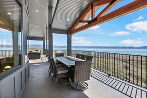 A covered outdoor dining area with a table and chairs, overlooking a scenic view of a body of water and distant mountains. - Private pool, hot tub, indoor basketball court, massive indoor slide, and VIEWS! (Bear Lake County)