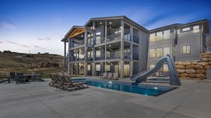Una casa de varios pisos con piscina, mobiliario exterior y un tobogán.