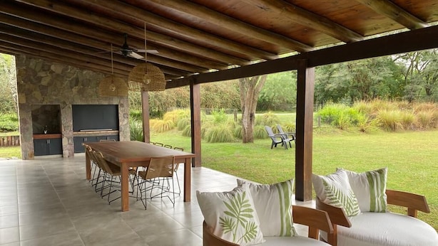 Une terrasse extérieure dotée d’une cheminée en pierre, d’une table à manger avec des chaises et d’un coin salon avec des coussins.