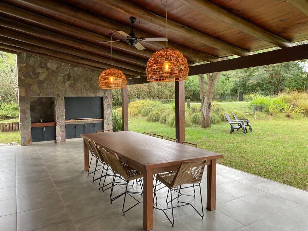 An outdoor patio with a stone fireplace, a wooden table with chairs, and hanging wicker lamps.