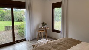 Une chambre à coucher avec un grand lit, une petite table sur laquelle est posée une plante, et une vue sur un jardin, visible à travers une porte coulissante.