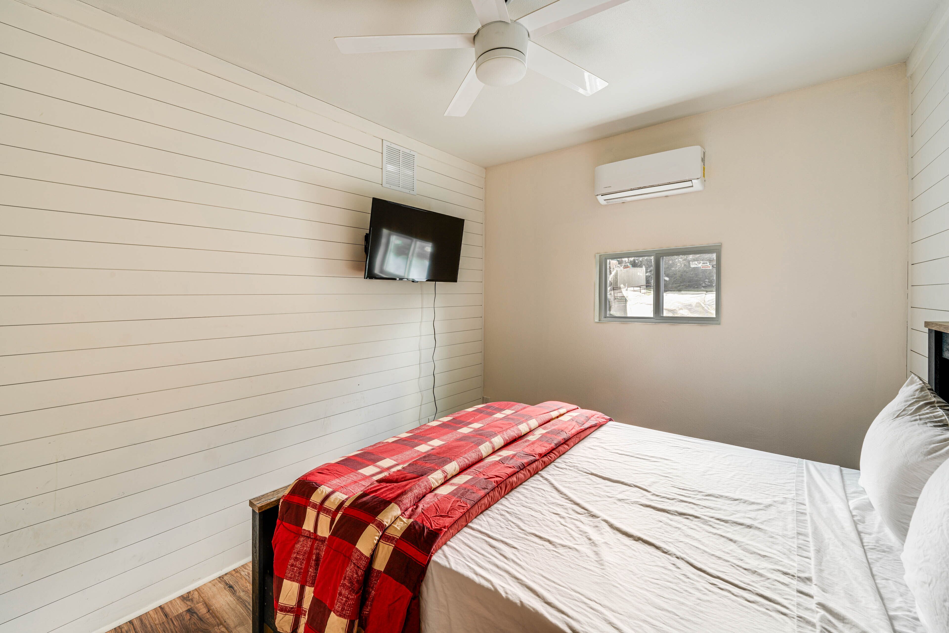 Une chambre à coucher comprenant un lit, un ventilateur de plafond, un téléviseur fixé au mur et un appareil de climatisation.