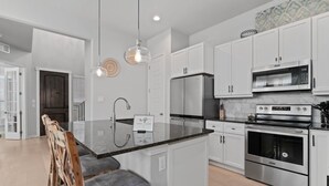 Une cuisine moderne avec des meubles blancs, un îlot central doté de tabourets, des appareils en acier inoxydable et un éclairage suspendu.