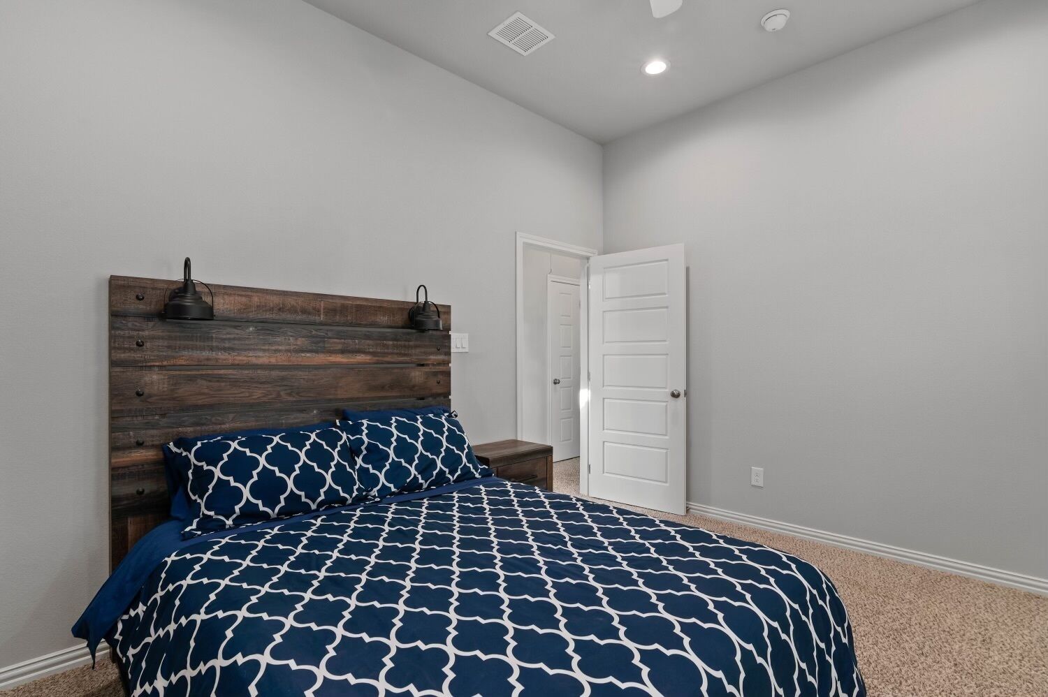 Une chambre à coucher avec une tête de lit en bois, une couvre-lit à motifs, une table de chevet et une porte blanche.