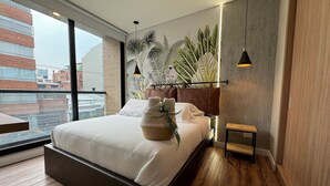 A modern bedroom with a large bed, a view of buildings through a window, and a plant wall.