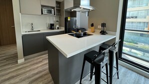 A modern kitchen with a central island, bar stools, a built-in oven, and a large window offering a view of the city.