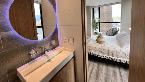 A modern bathroom with a large mirror, a white sink, and a wooden vanity.
