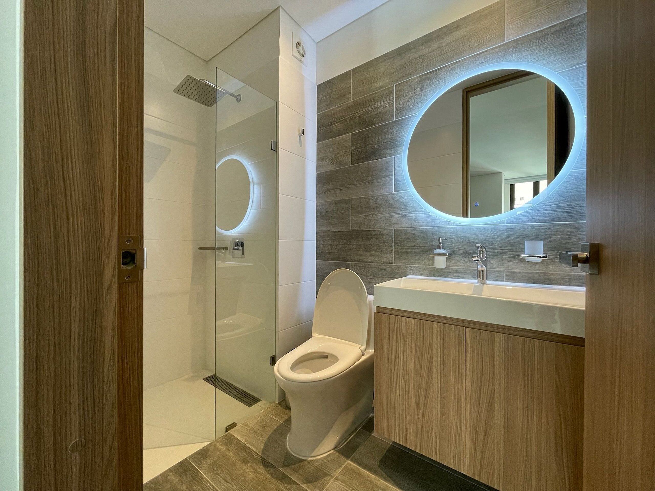 Une salle de bain moderne avec une douche à parois de verre, des toilettes et un meuble-lavabo avec un miroir.
