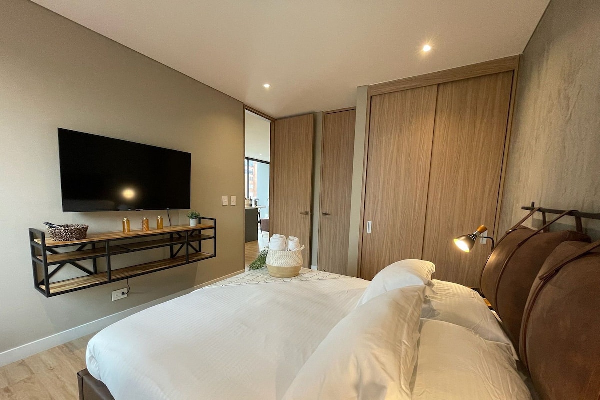 A bedroom with a bed, a TV mounted on the wall, a bedside table, and a wardrobe.