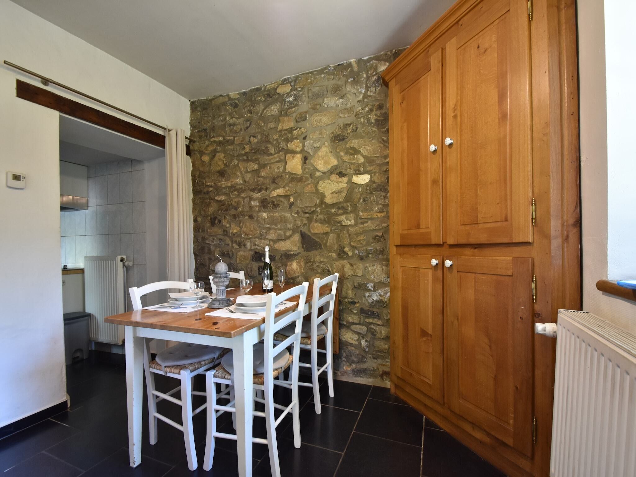 A dining area with a stone wall, a wooden cabinet, and a kitchen in the background.