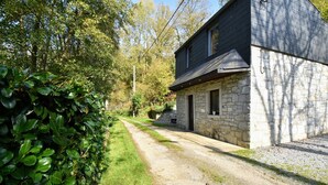 A rustic stone building with a dark roof, a gravel driveway, and lush greenery. - Cottage with Bubble Bath (Clavier (les Avins))