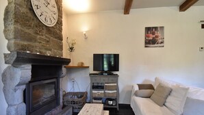 A cozy living room with a stone fireplace, a television, a white sofa, and a framed picture on the wall. - Cottage with Bubble Bath (Clavier (les Avins))