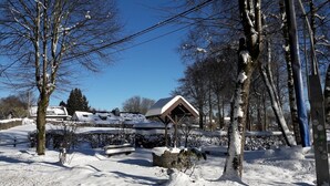 A snow-covered landscape with a building featuring a sloped roof and a small pavilion. - Holiday Home with Garden, Heating, Barbecue (Butgenbach)