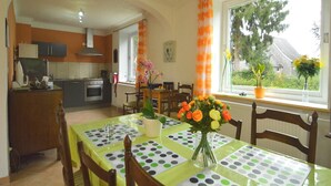 A dining area with a table set for two, a vase of flowers, and a view of the outdoors through a window. - Holiday Home with Garden, Heating, Barbecue (Butgenbach)