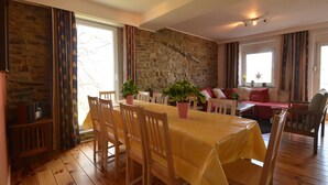 Un comedor con pared de piedra, sillas de madera, una mesa con mantel amarillo y plantas en macetas.