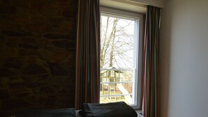 Un dormitorio con pared de piedra, cama con colcha estampada floral y ventana con cortinas a rayas.
