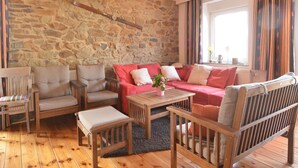Una sala de estar acogedora con pared de piedra, un sofá rojo, muebles de madera y una ventana con cortinas.