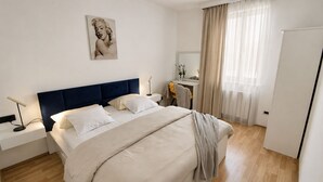 Une chambre à coucher comprenant un lit, des tables de chevet, un bureau, une chaise, un miroir et un tableau accroché au mur.