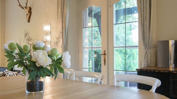A dining area with a wooden table, white chairs, a vase of flowers, and a deer skull on the wall.