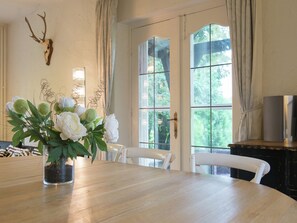 A dining area with a wooden table, white chairs, a vase of flowers, and a deer skull on the wall. - Mansion in Spa Liege with private garden (Spa)