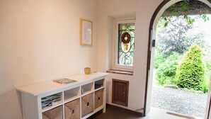 A hallway with a white console table, wicker baskets, a door, and a window with a wreath.