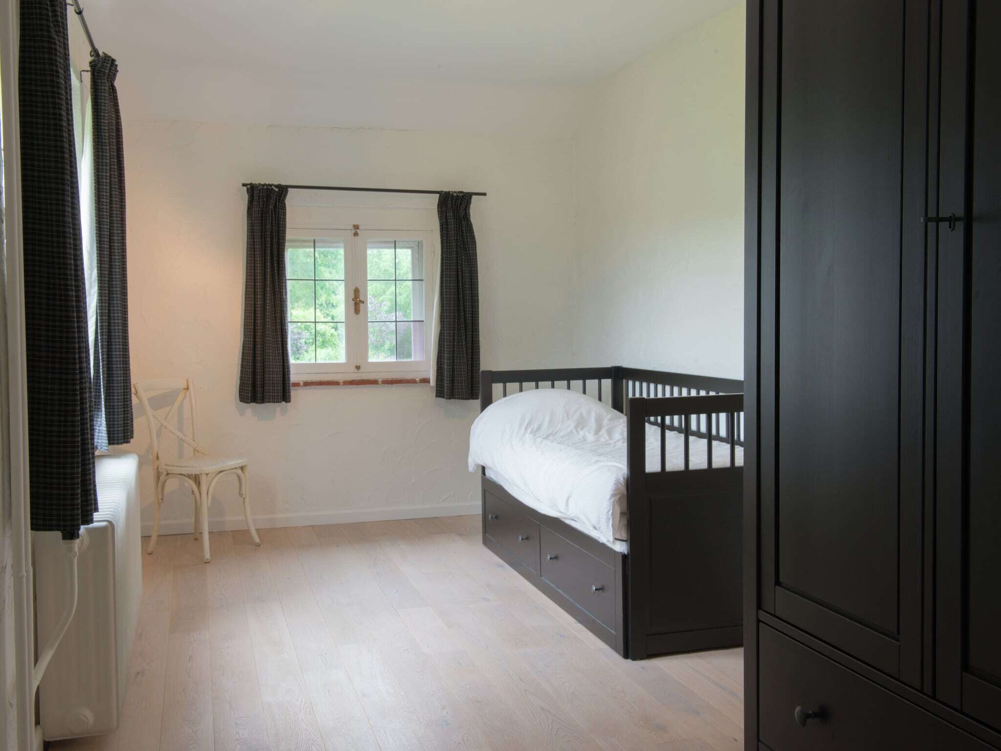 Une chambre avec un lit simple, une chaise, un radiateur et une fenêtre avec des rideaux.