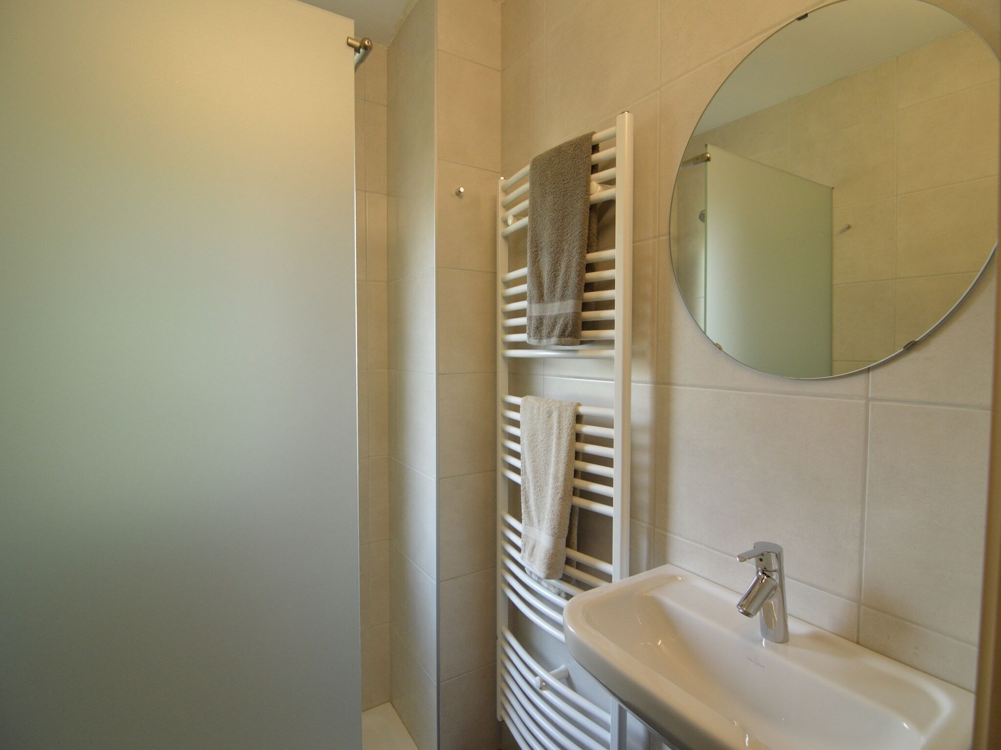 A bathroom with a white sink, a mirror, and two towel racks with towels.