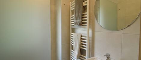 A bathroom with a white sink, a mirror, and two towel racks with towels.