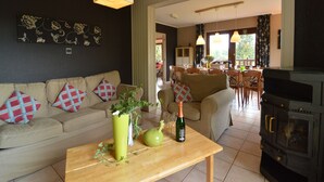 A living room with a sofa, a wooden table with a vase and a bottle, and a kitchen area with a stove. - Ondenval Stay with Sauna (Waimes-Ondenval)