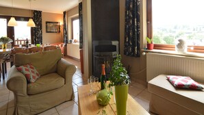 A living room with a sofa, a coffee table with a vase and wine glasses, a fireplace, and a window with a view. - Ondenval Stay with Sauna (Waimes-Ondenval)