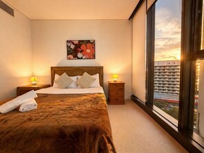 A bedroom with a large bed, two bedside tables with lamps, a window with a city view, and a floral artwork on the wall. - The City Pad-2B-Central CBD-Skytower C17 (Brisbane City)