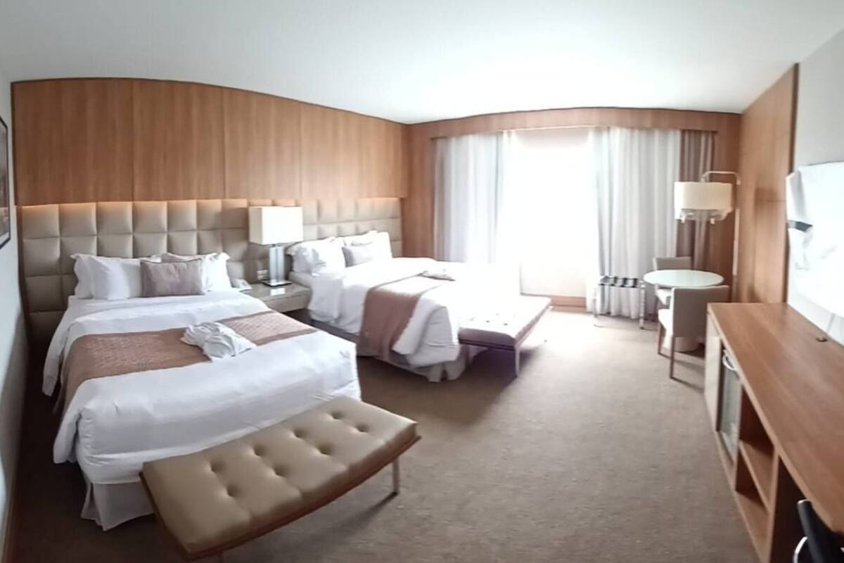 Ein Hotelzimmer mit zwei Betten, einer Sitzecke, einem Schreibtisch, einem Fernseher und einem Fenster mit Vorhängen.
