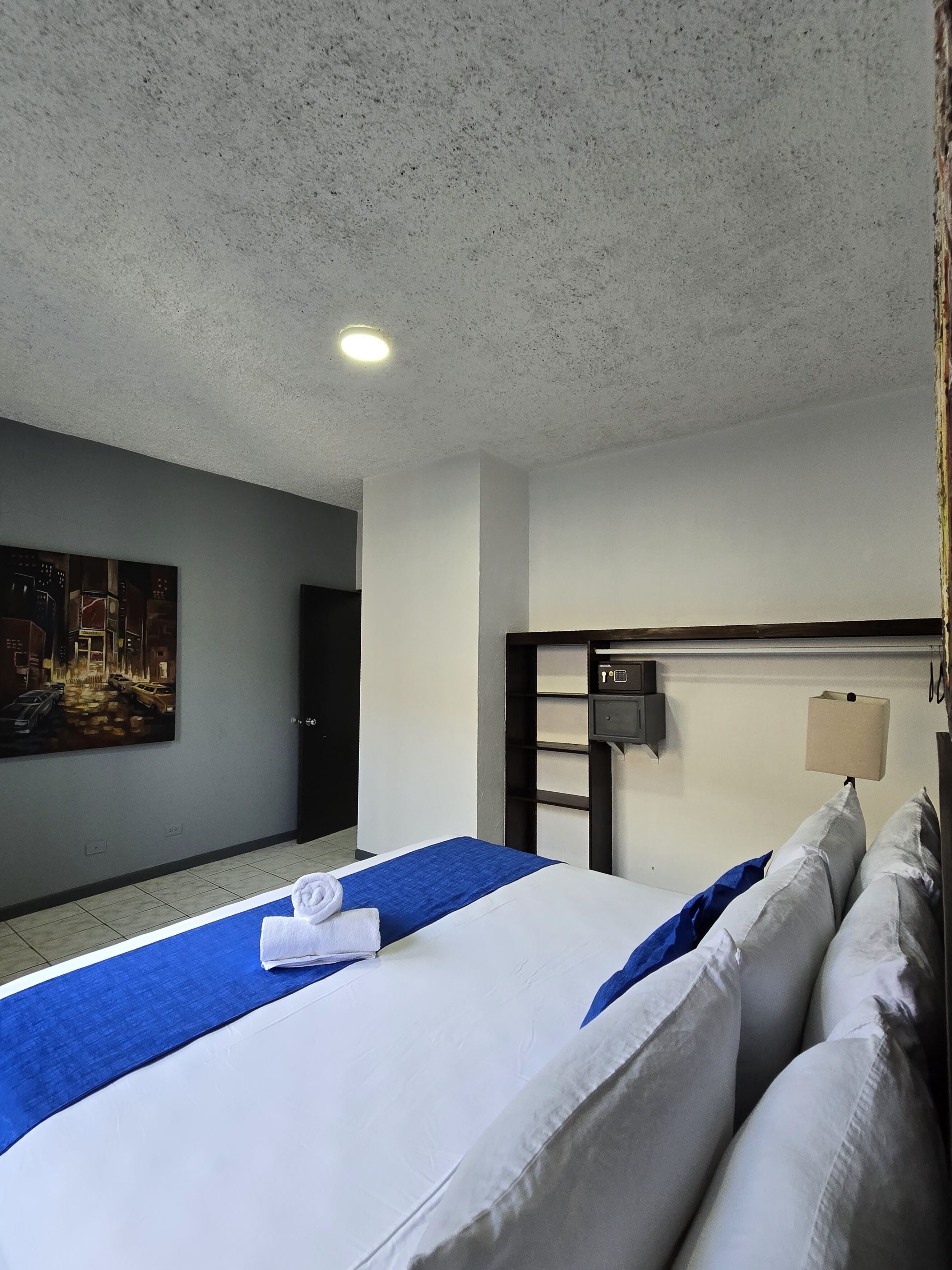 A hotel room with a large bed, a painting on the wall, a small desk, and a nightstand.