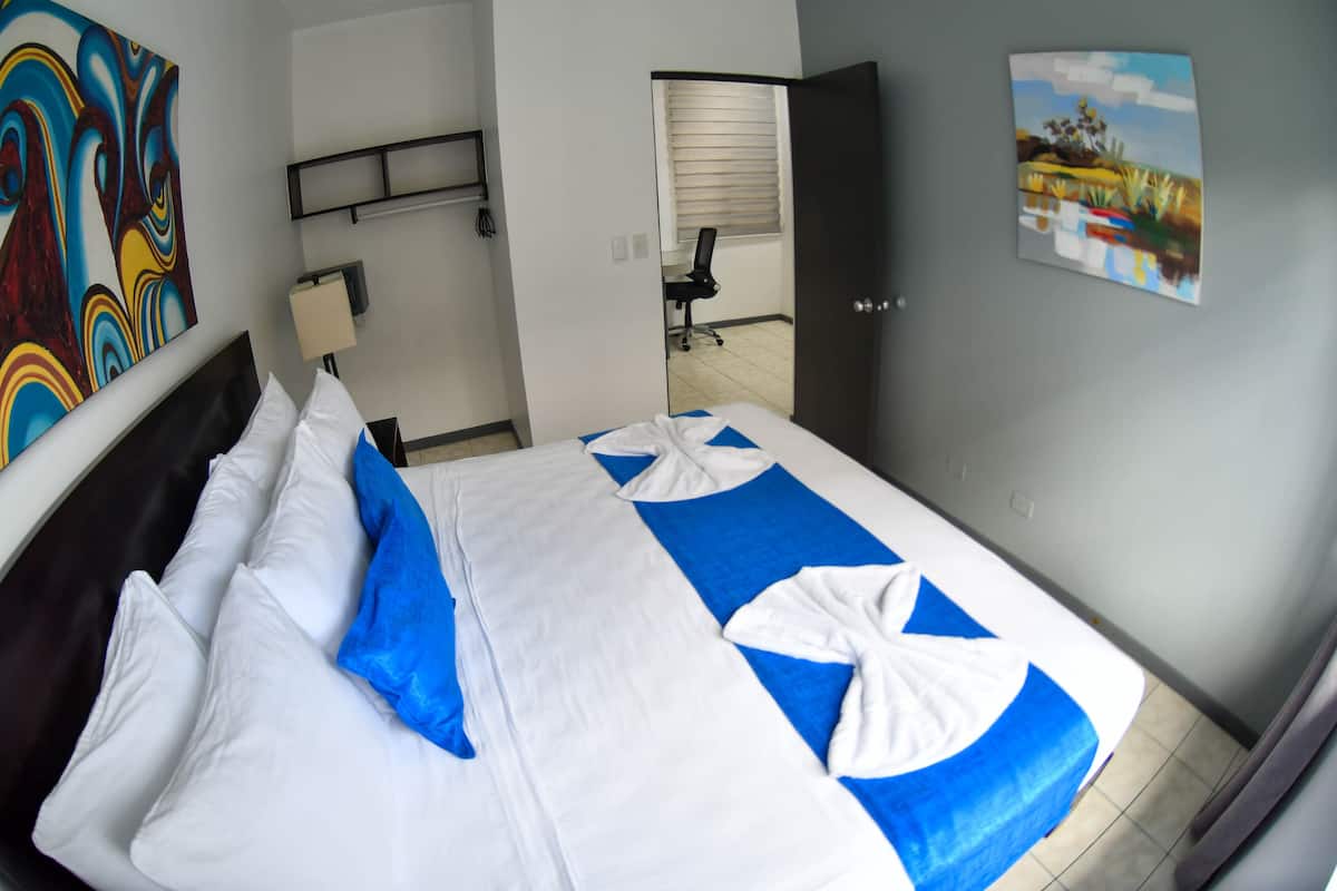 A hotel room with a bed, a desk, a chair, and a painting on the wall.