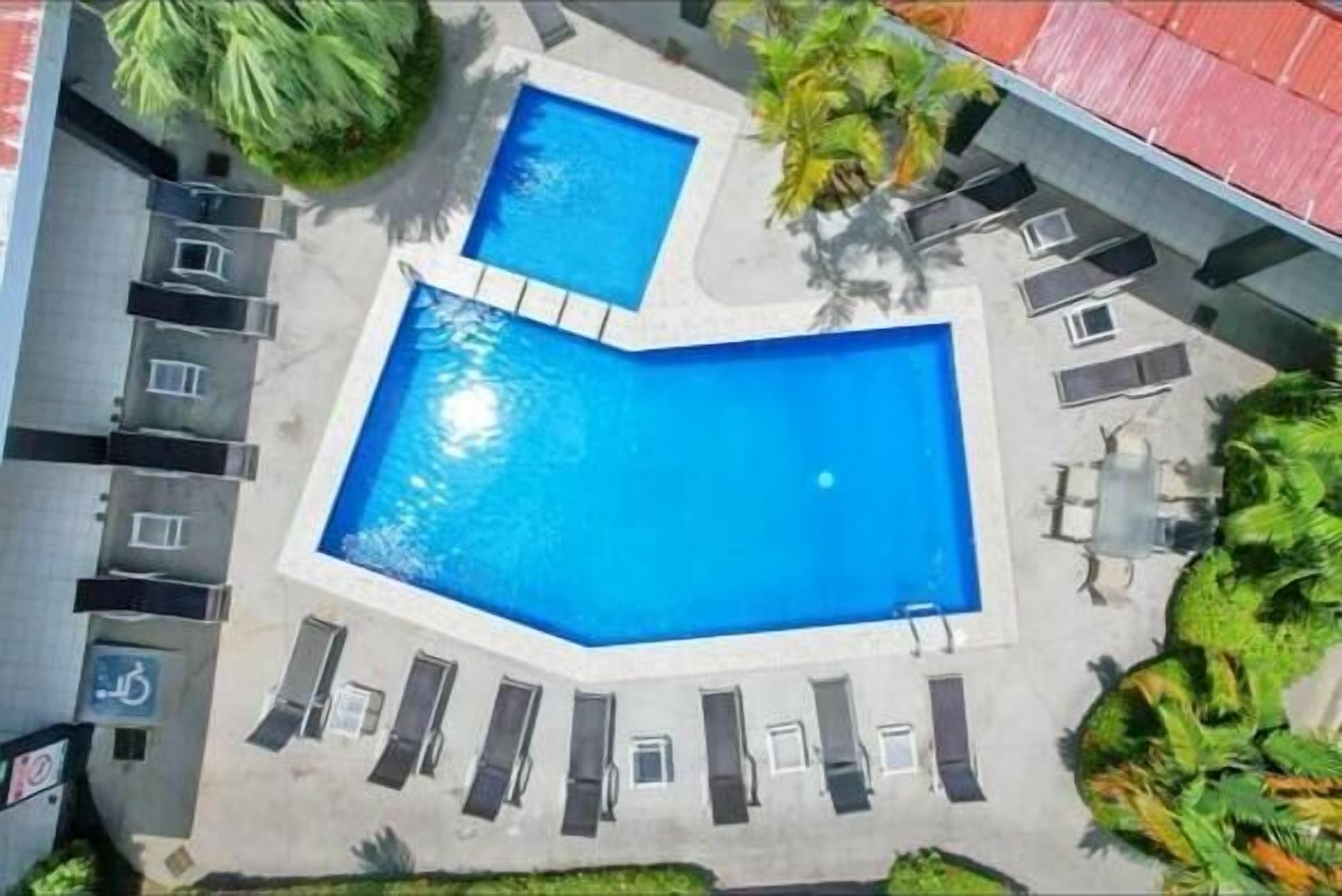 Un espace piscine aménagé sur le toit, comprenant deux piscines, des chaises longues et un petit jardin.