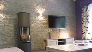 Een moderne woonkamer met een stenen muur, een flatscreen televisie boven een houten console, een open haard, en een eethoek met een tafel en stoelen.