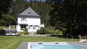 Een huis met een zwembad, omringd door een verzorgd gazon en bomen.