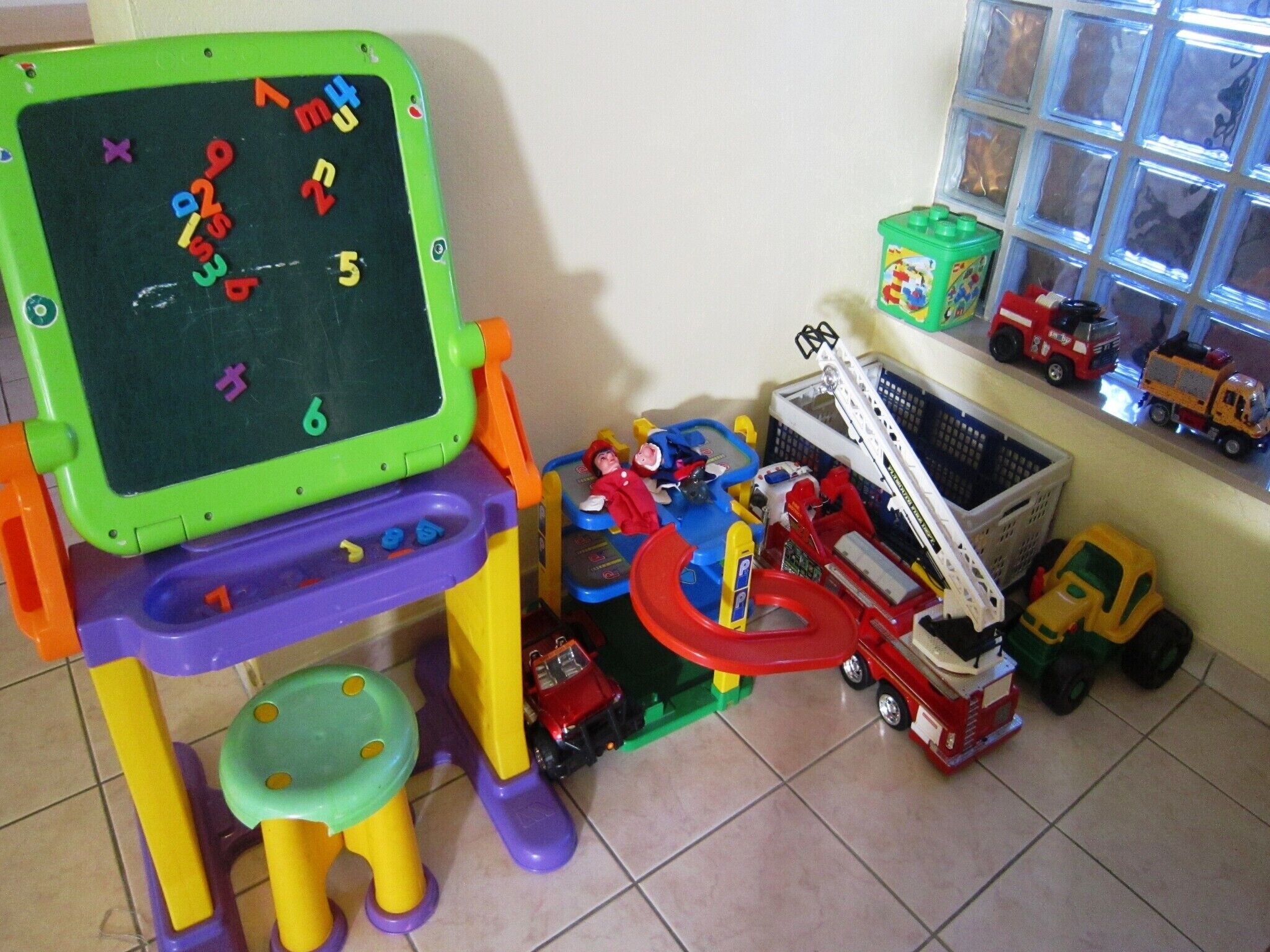 A play area with a green chalkboard, toy vehicles, and a toy crane.