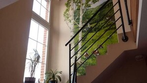 A staircase with a black handrail, a mural of a tree and landscape, and potted plants on the landing. - Spacious Baugnez Cottage (Malmedy-Baugnez)