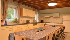 A spacious kitchen with a long dining table, wooden cabinets, and a built-in microwave. - Family Cottage with Sauna (Malmedy-Baugnez)