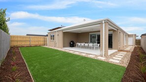 A covered patio area with a barbecue grill, outdoor seating, and a well-maintained lawn.