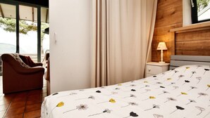 A bedroom with a bed, a chair, a nightstand, a lamp, and a window with curtains.