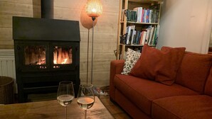 A cozy living room with a wood-burning stove, a red sofa, a bookshelf, and two glasses of white wine on a wooden table.